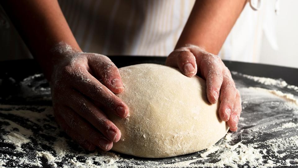Photograph of a baker kneading dough. Their hands are covered in flour
