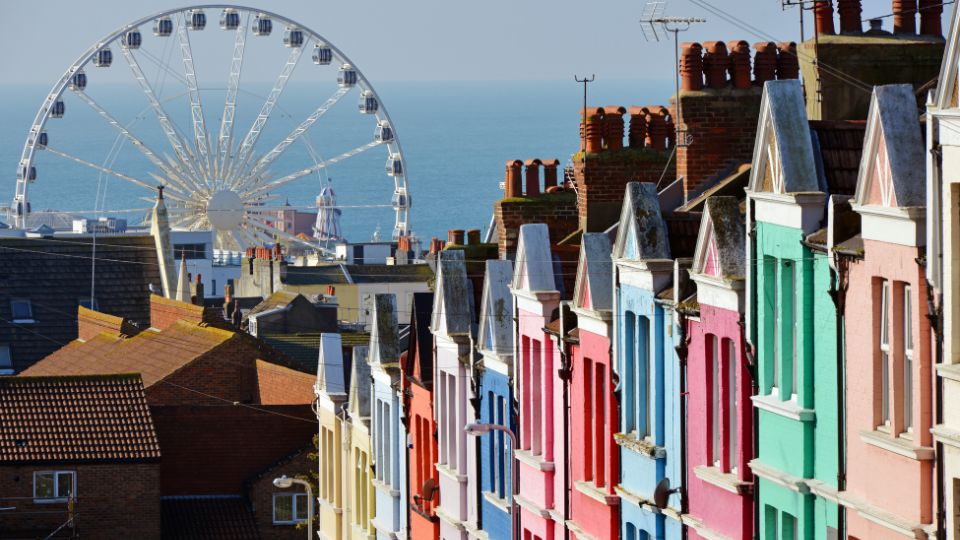 A photograph of Brighton. There are multicoloured houses and a ferris wheel. The sea is in the background.