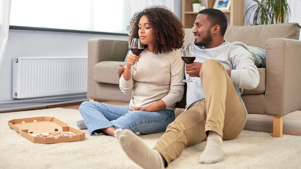 Couple drinking wine and eating pizza on the floor of their living room