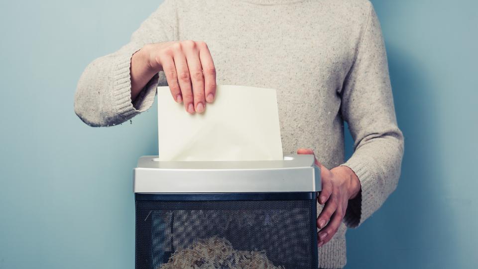 A photograph of a man putting confidential documents through a paper shredder