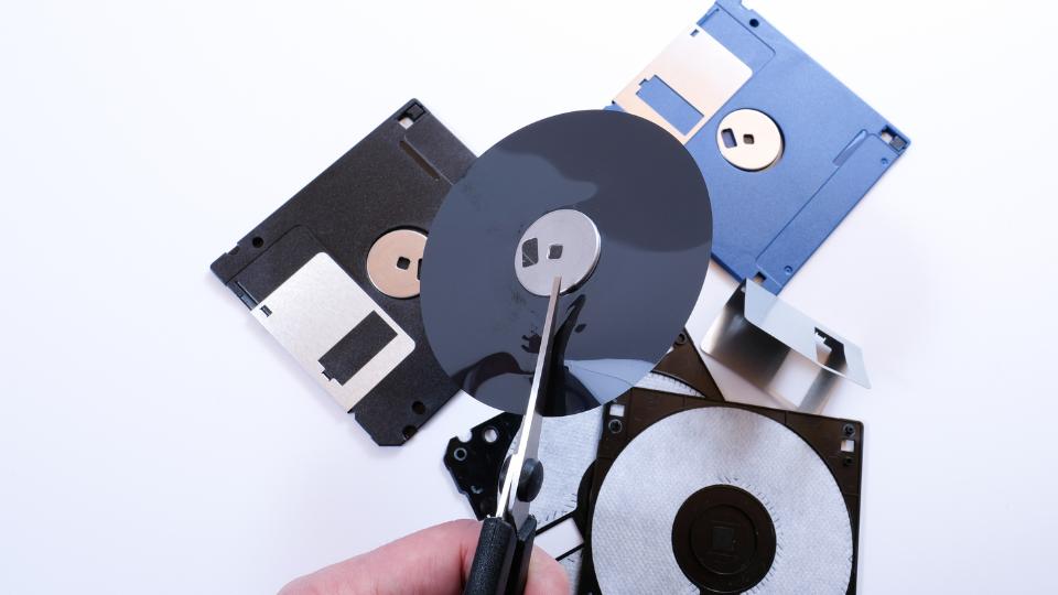 A photograph of someone cutting up storage devices including floppy disks and cds. This is being done to avoid data breaches.