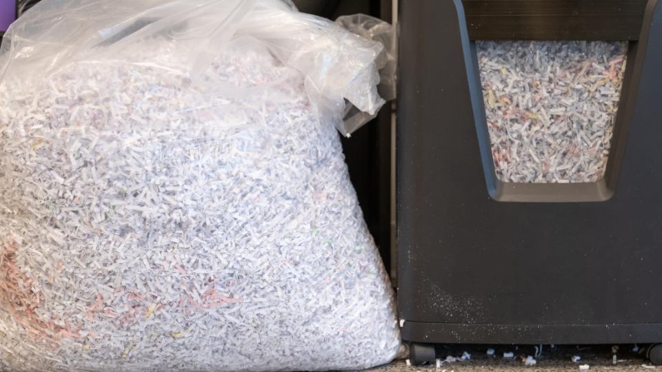 A photograph of some confidential waste paper in a clear bin bag next to a paper shredder