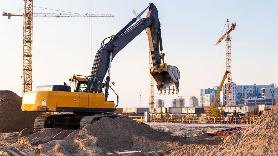 A picture of a digger and crane at a construction site