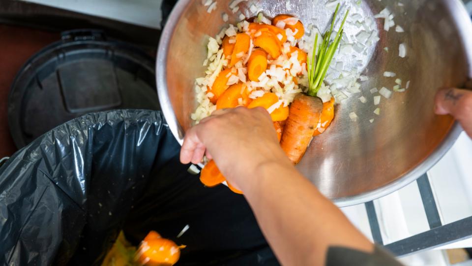 A photograph of an employee disposing of food waste into a food waste bin.