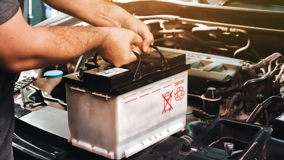 A photograph of a car battery being put into an engine