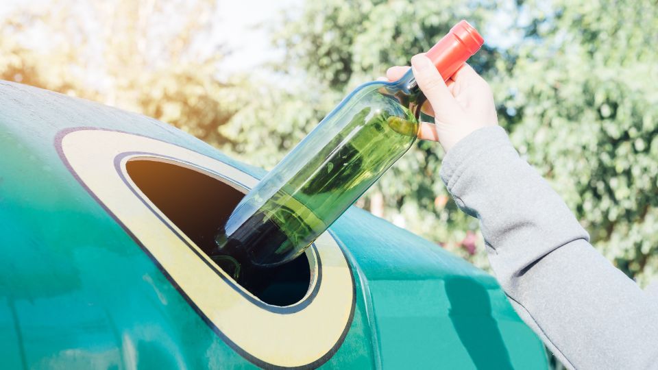 A photograph of a women recycling an old glass wine bottle