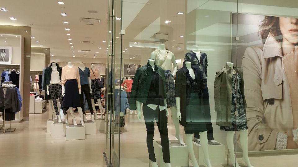 A photograph of a clothing retail store with lots of plastic mannequins in the window and on the shop floor. 