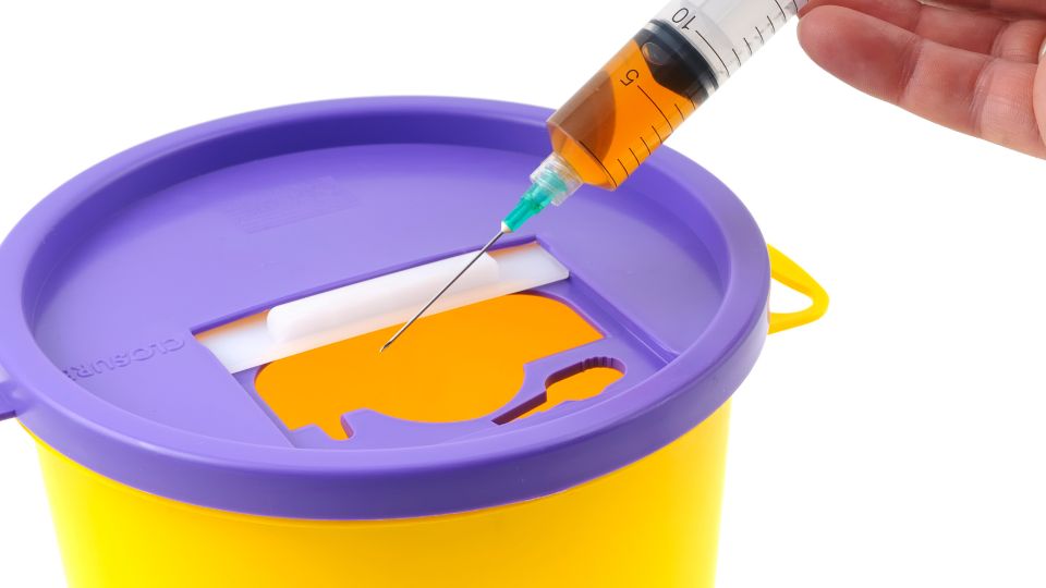 photograph of someone putting sharps waste in a special bin