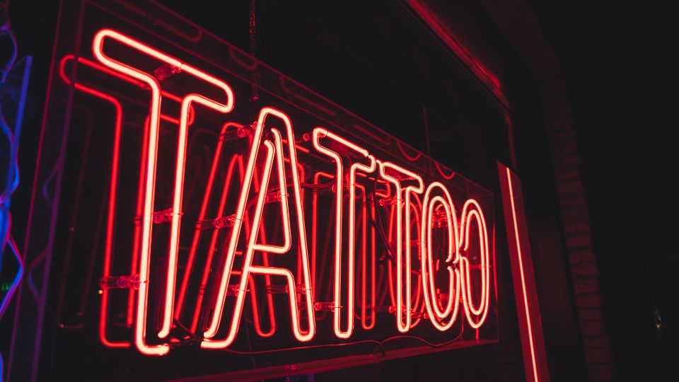 A photograph of a neon tattoo sign in a tattoo parlour.
