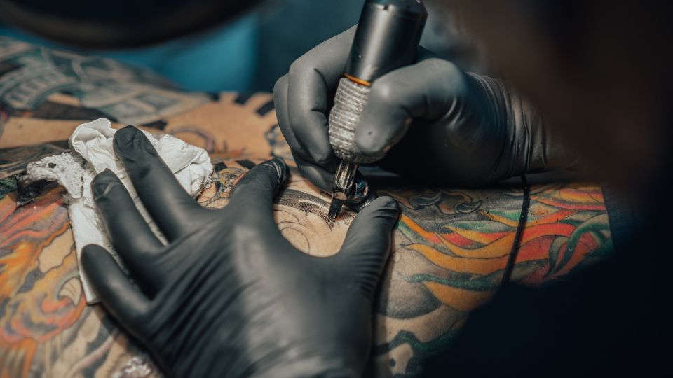 A photograph of a tattoo artist giving someone a tattoo with coloured ink