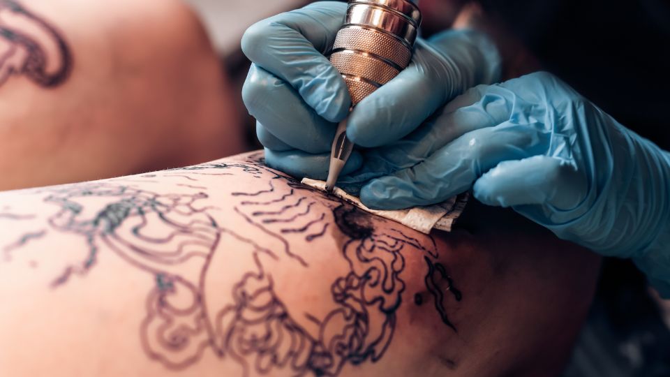 photograph of a tattoo artist giving someone a tattoo in black ink