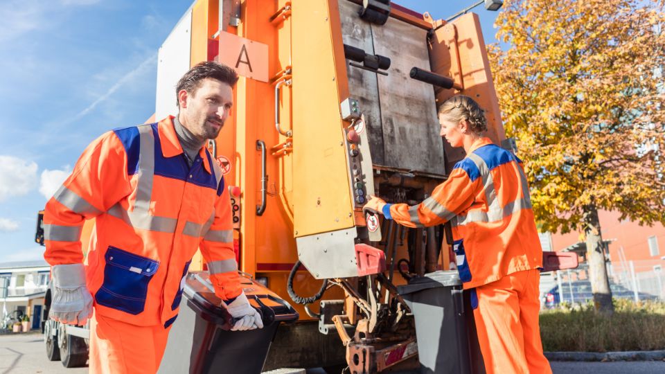 Two workers collecting waste from wheelie bins and putting it inot an orange waste truck