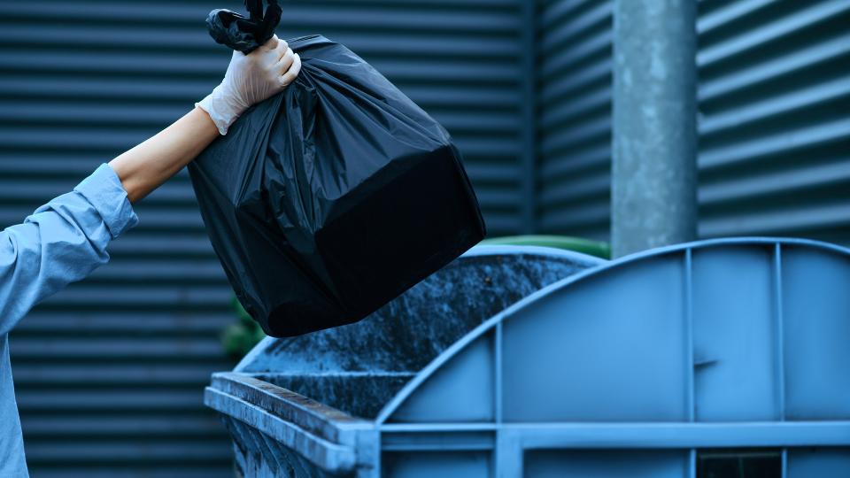 Commercial general waste in a black bin bag being put into large blue wheelie bin