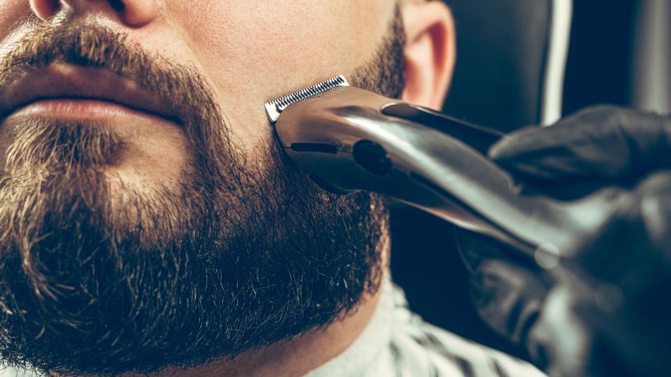 a barber shaving a mans beard with an electric razor