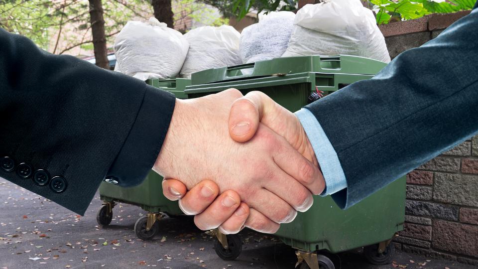 Shaking hands next to a large business wheelie bin